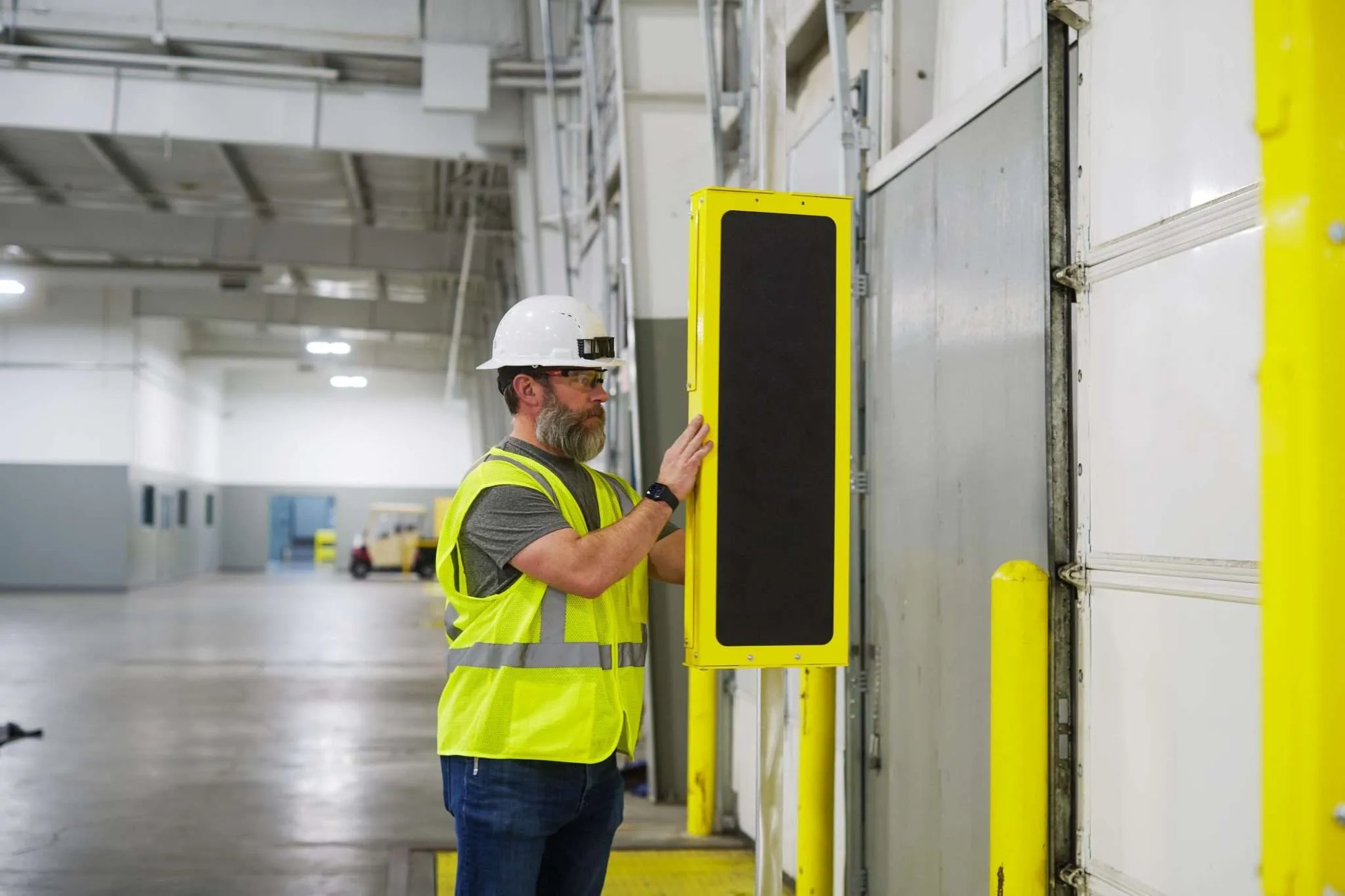 Person in a warehouse wearing a safety vest and hard hat, interacting RFID U-Bolt pole mount for EasyPort Flex antenna installation